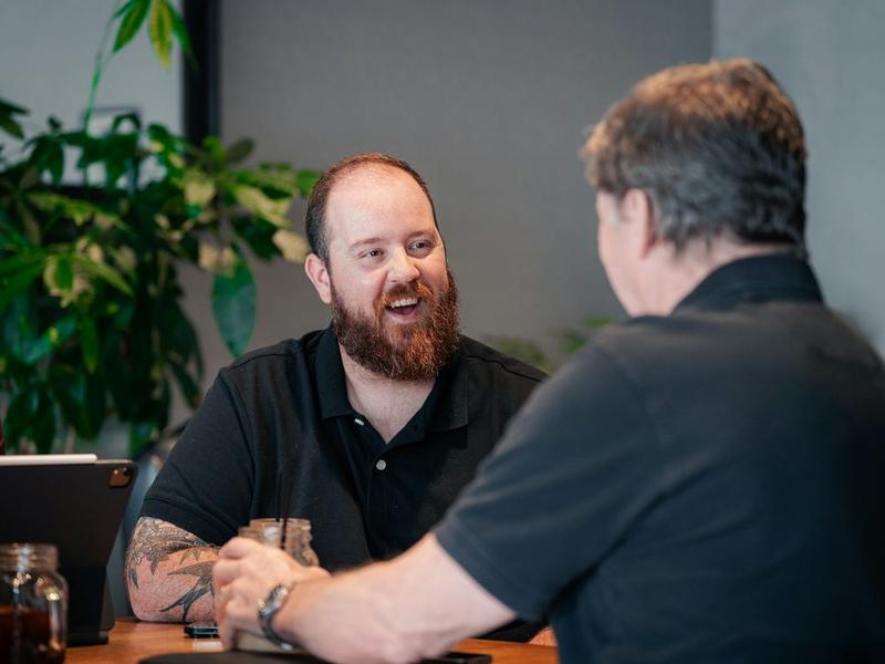 Un tatoueur explique son travail à un client, assis à une table.