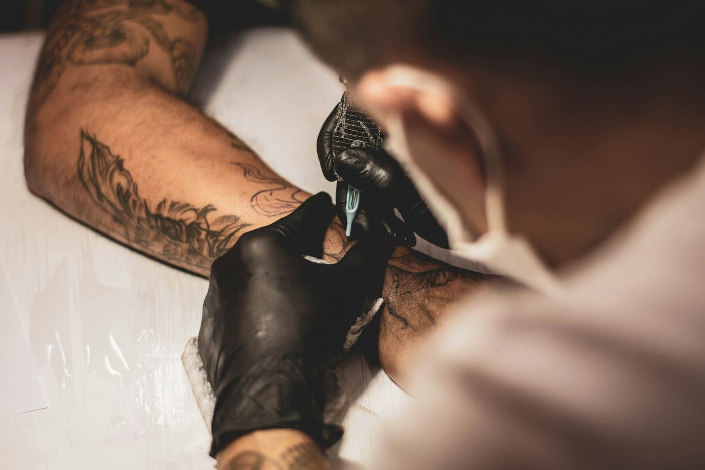 Des mains gantées de noir tatouent un avant-bras.